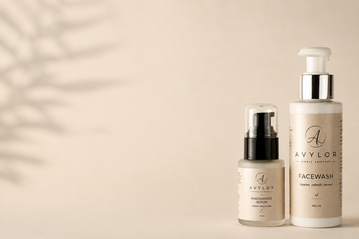 Two skincare products from Avylor on a warm beige background with soft leaf shadows: a small bottle of facial cleanser with a black pump and a larger bottle of facewash with a white pump and silver collar.